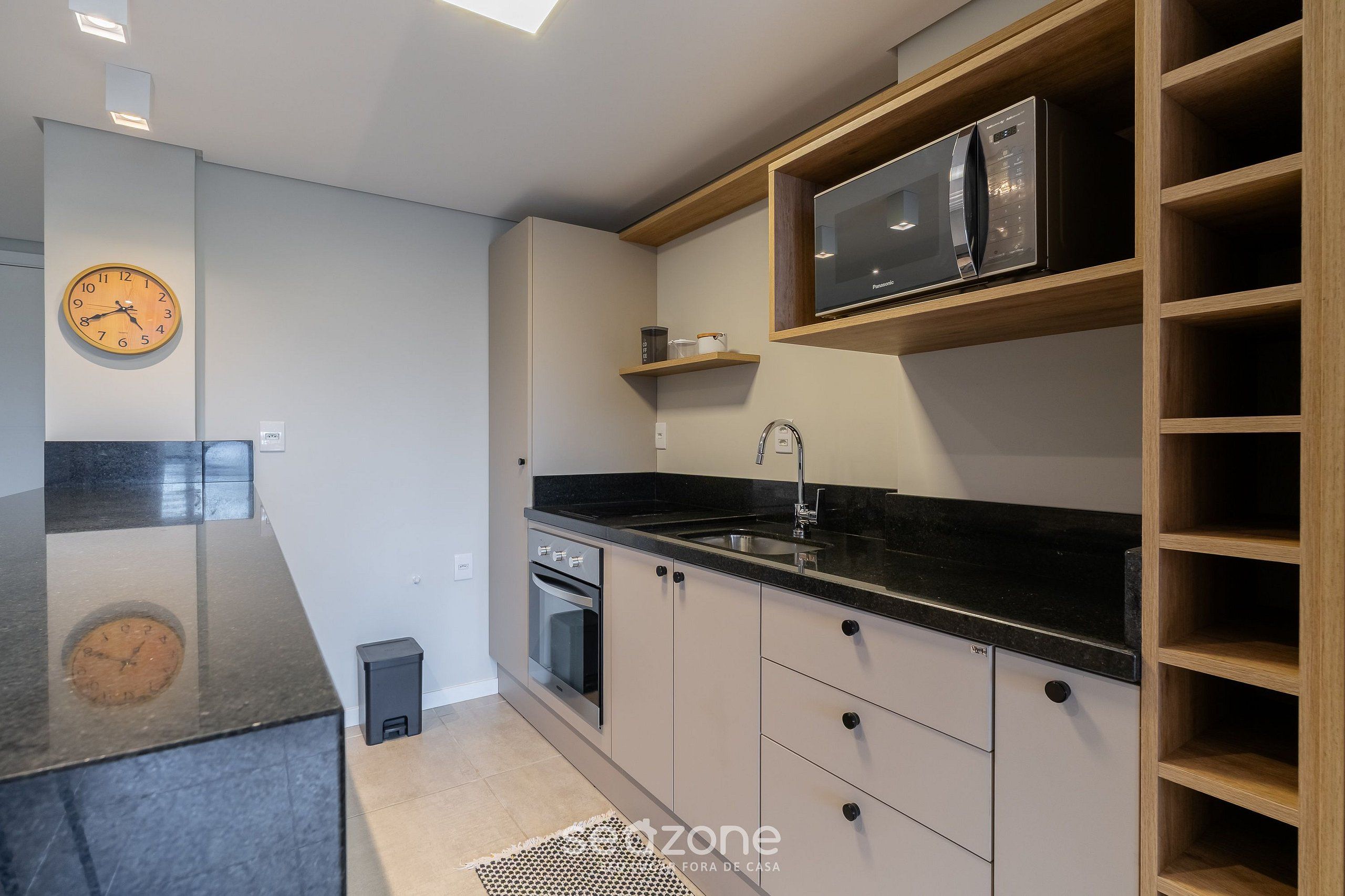 A modern kitchen with a black countertop, stainless steel appliances, and wooden shelving.