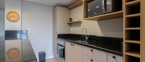 Una cocina moderna con encimera negra, electrodomésticos de acero inoxidable y estanterías de madera.