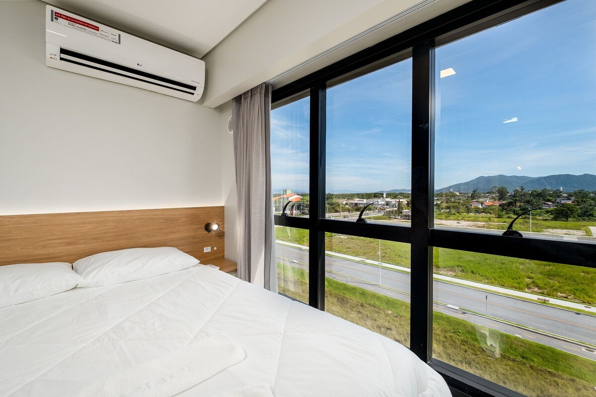 Hotelkamer met een groot bed, een airconditioning en een raam met uitzicht op een snelweg en bergen.