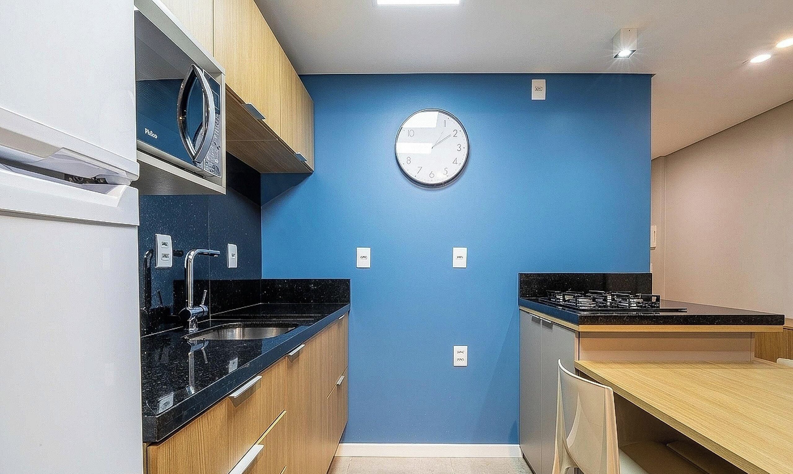 A compact kitchen with a blue wall, a round clock, and modern appliances.