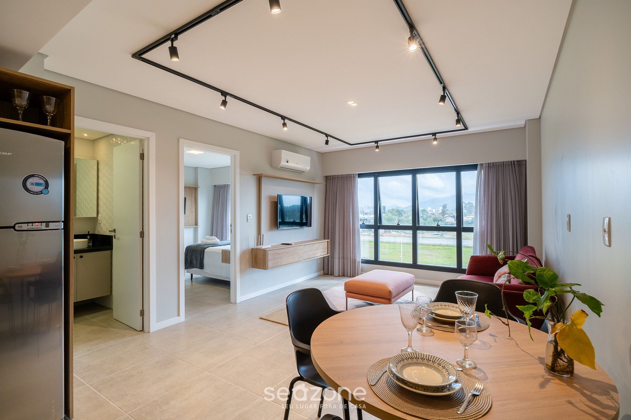 Uma sala de estar moderna com área de jantar, cozinha e TV na parede.