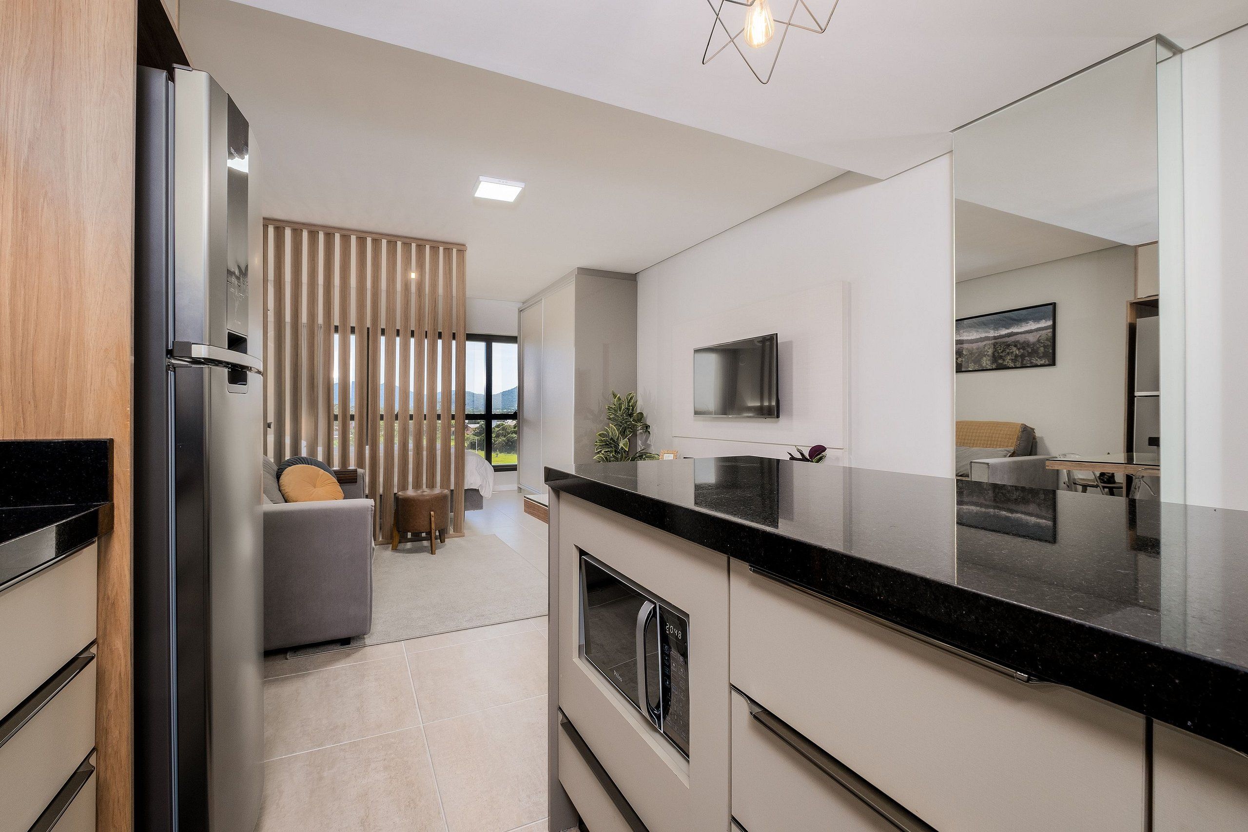A modern kitchen with a built-in oven, a large black countertop, and a TV mounted on the wall.