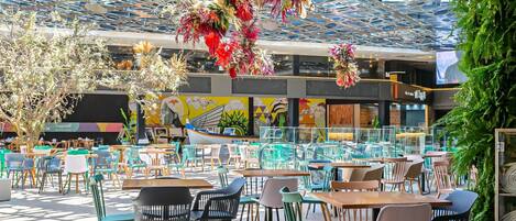 Un comedor interior con varias mesas y sillas, un mural colorido y un diseño de techo único.