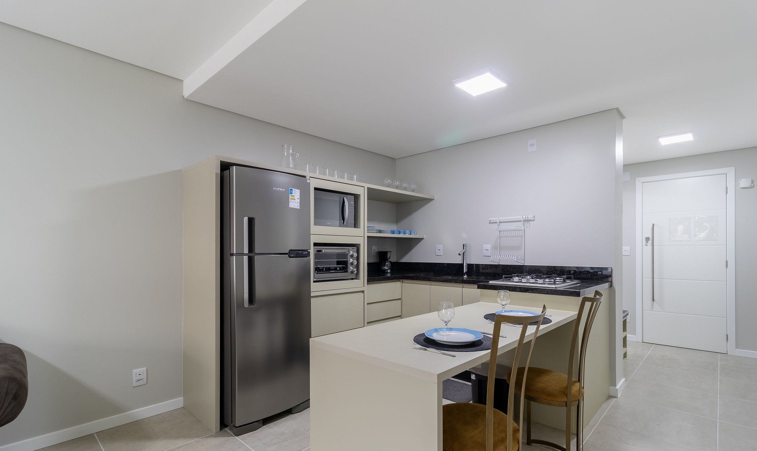 Una cocina moderna con refrigerador, horno y microondas integrados. Hay una mesa de comedor con sillas y una pequeña isla.
