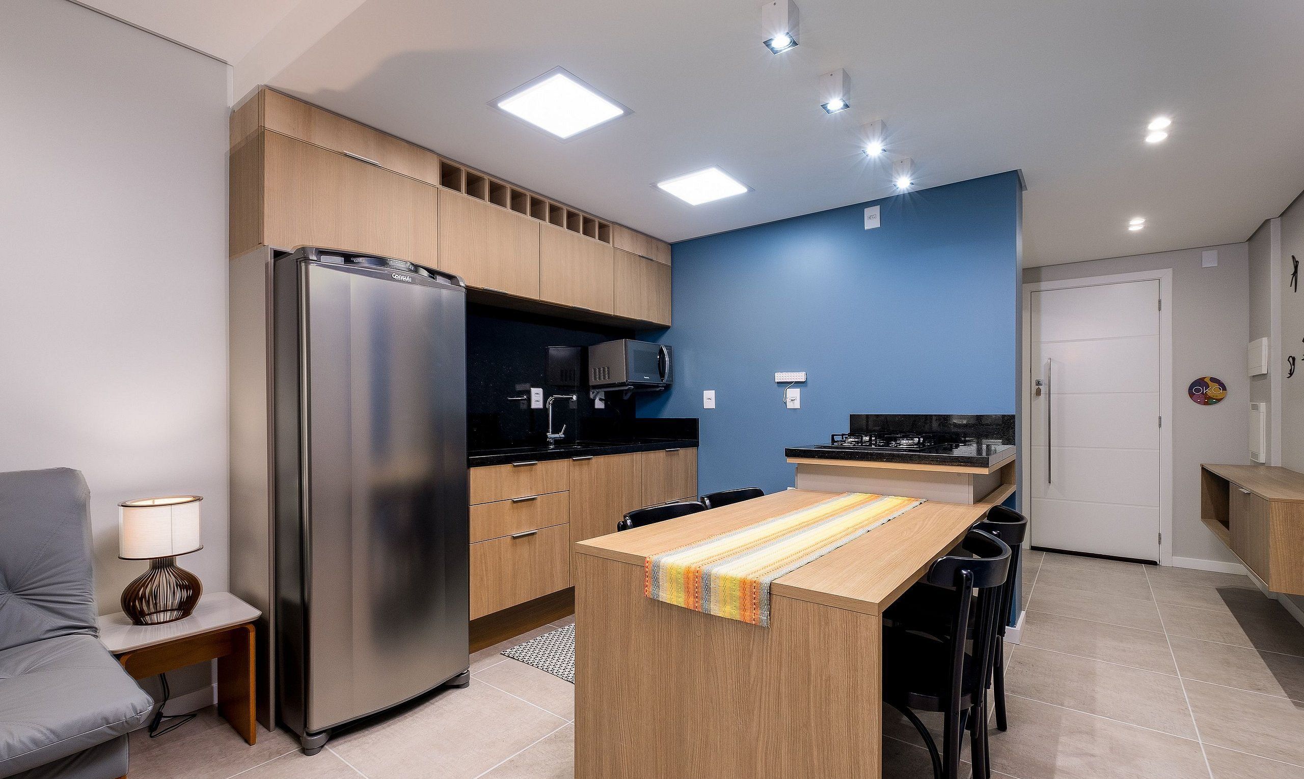 Una cocina compacta con refrigerador, microondas y estufa, gabinetes de madera y un pequeño comedor con sillas.