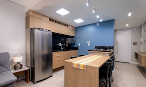 Une cuisine compacte équipée d’un réfrigérateur, d’un four à micro-ondes et d’une cuisinière, avec des armoires en bois et un petit coin repas comprenant des chaises.
