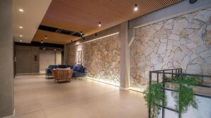 A modern lobby with a stone wall, a seating area with a sofa and chairs, and a wooden ceiling. - OKA Floripa (Florianópolis)