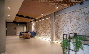Een moderne lobby met een stenen muur, een zithoek met een bank en stoelen, en een houten plafond.