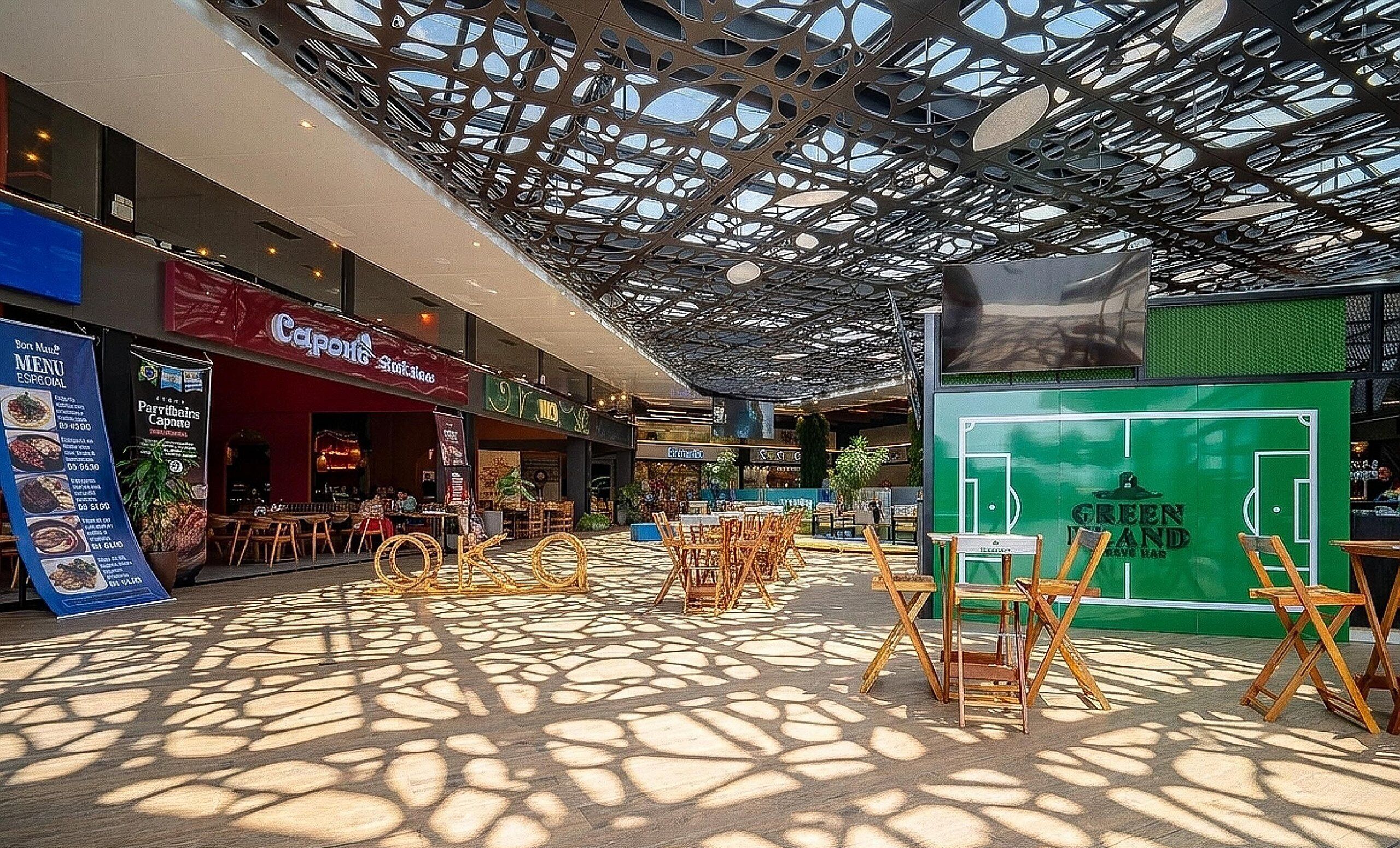 Interior moderno de um shopping com teto estampado, área de estar ao ar livre e diversas lojas.