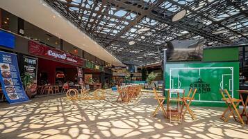 Interior moderno de um shopping com teto estampado, área de estar ao ar livre e diversas lojas.