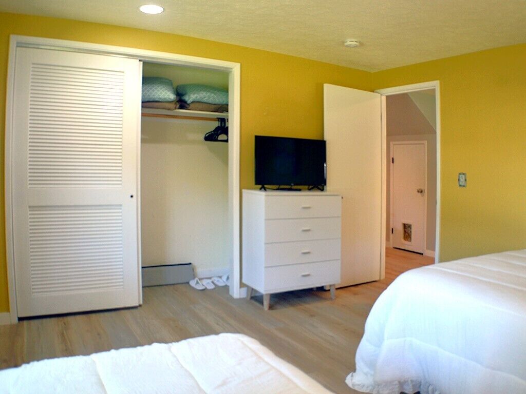 Un dormitorio con una cama, un televisor sobre un aparador, un armario y una puerta que da a otra habitación.