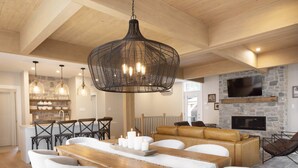 Ett rymligt matområde med ett träbord och vita stolar, en stor, vävd lampa och en stenkamin i bakgrunden.