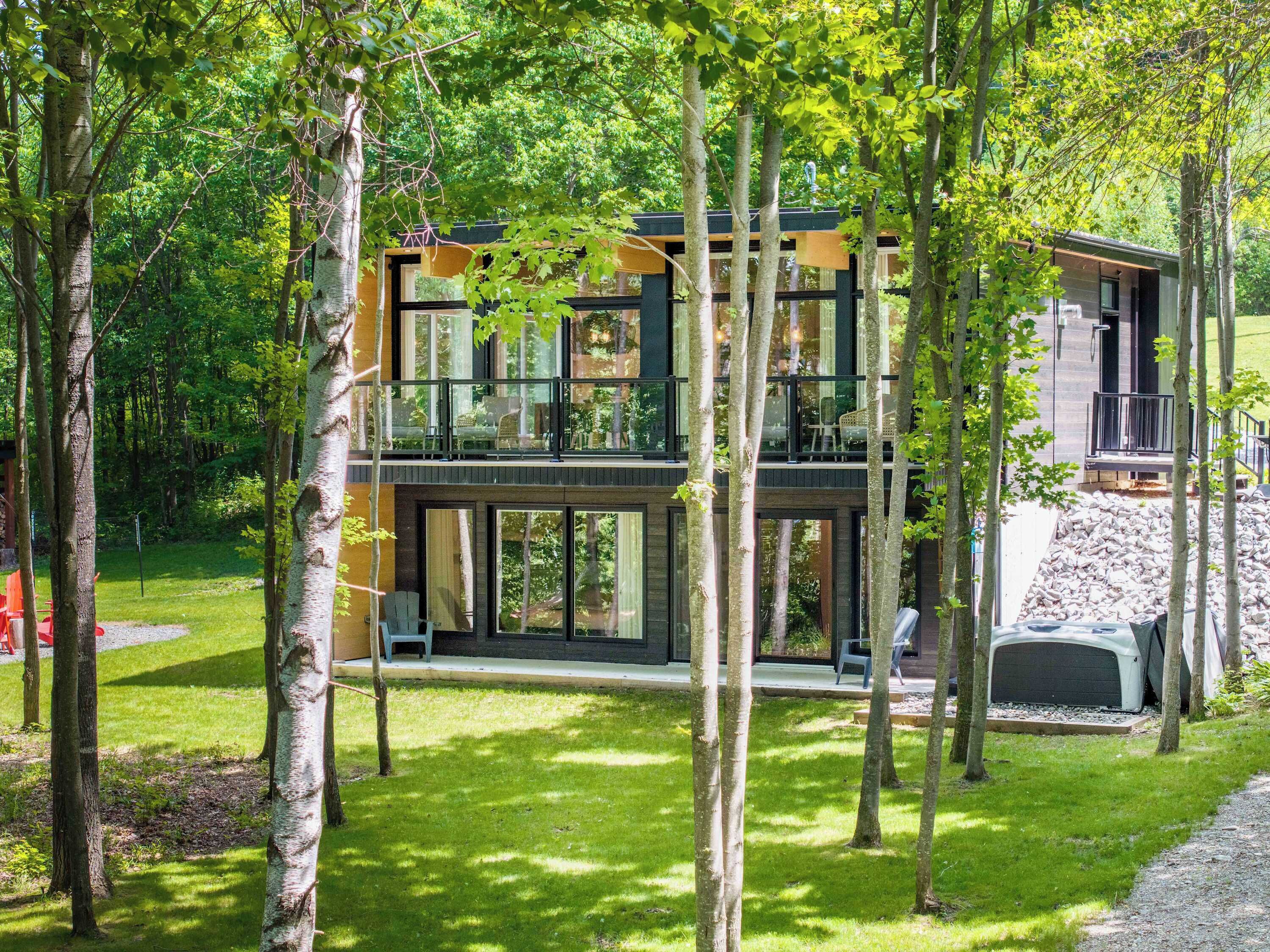 Une maison moderne à deux étages, dotée de grandes fenêtres et entourée d’arbres.