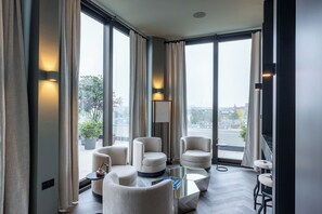 A modern hotel room with large windows, a sofa set, a coffee table, and a view of the city.