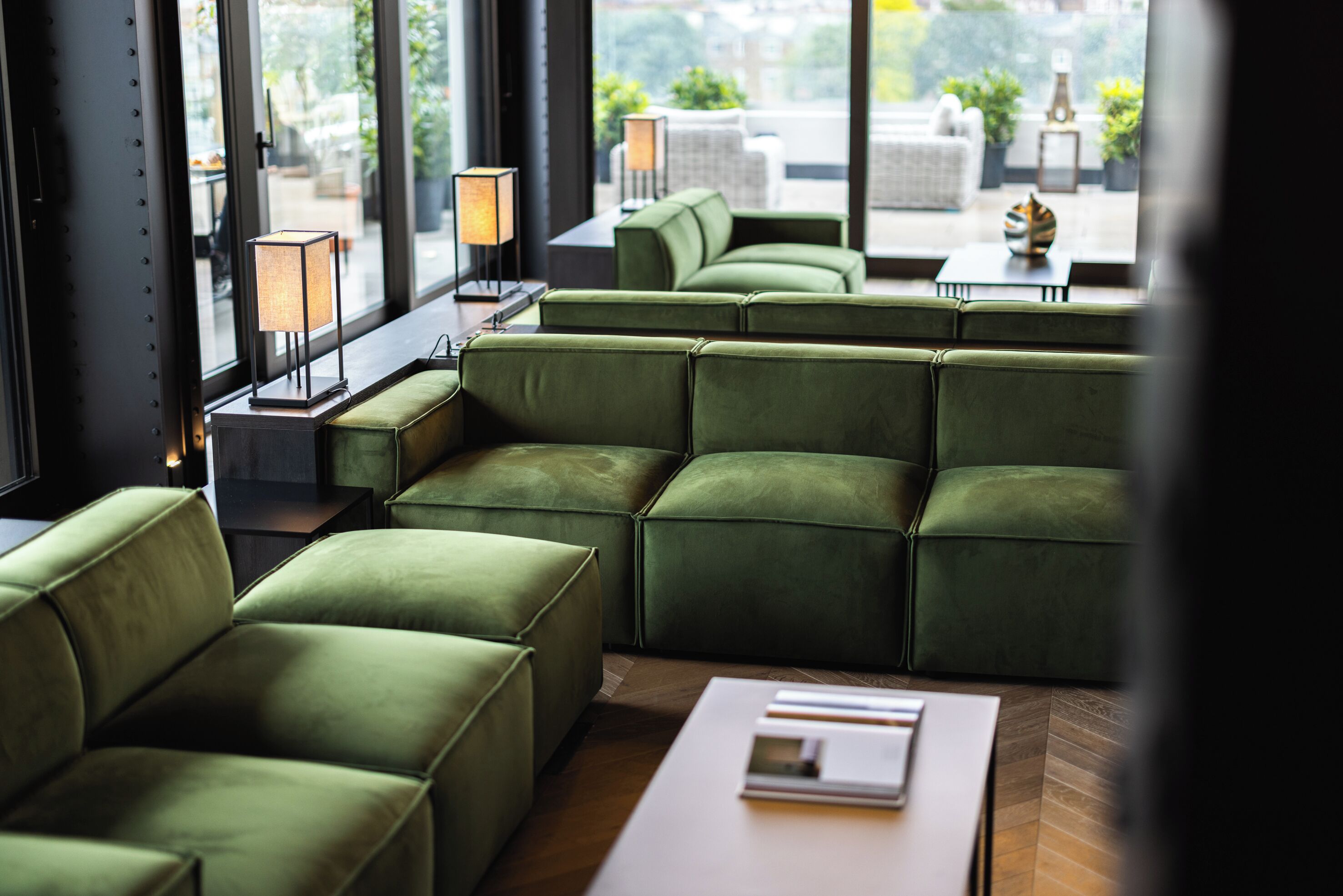 A green upholstered seating area with a view of the outdoors through large windows.
