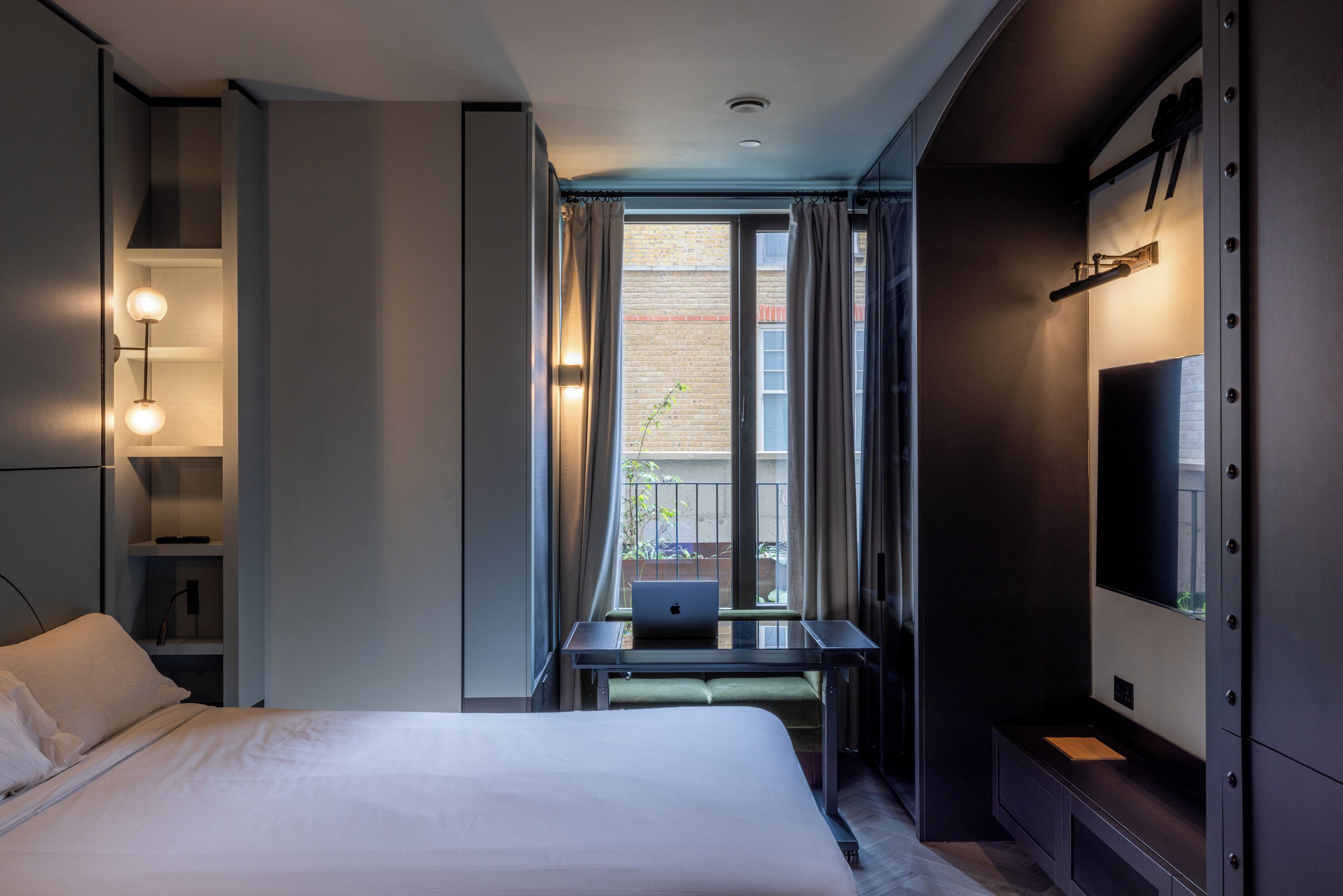Une chambre d  ’hôtel avec un lit, un bureau avec un ordinateur portable, une télévision et un balcon avec des rideaux.