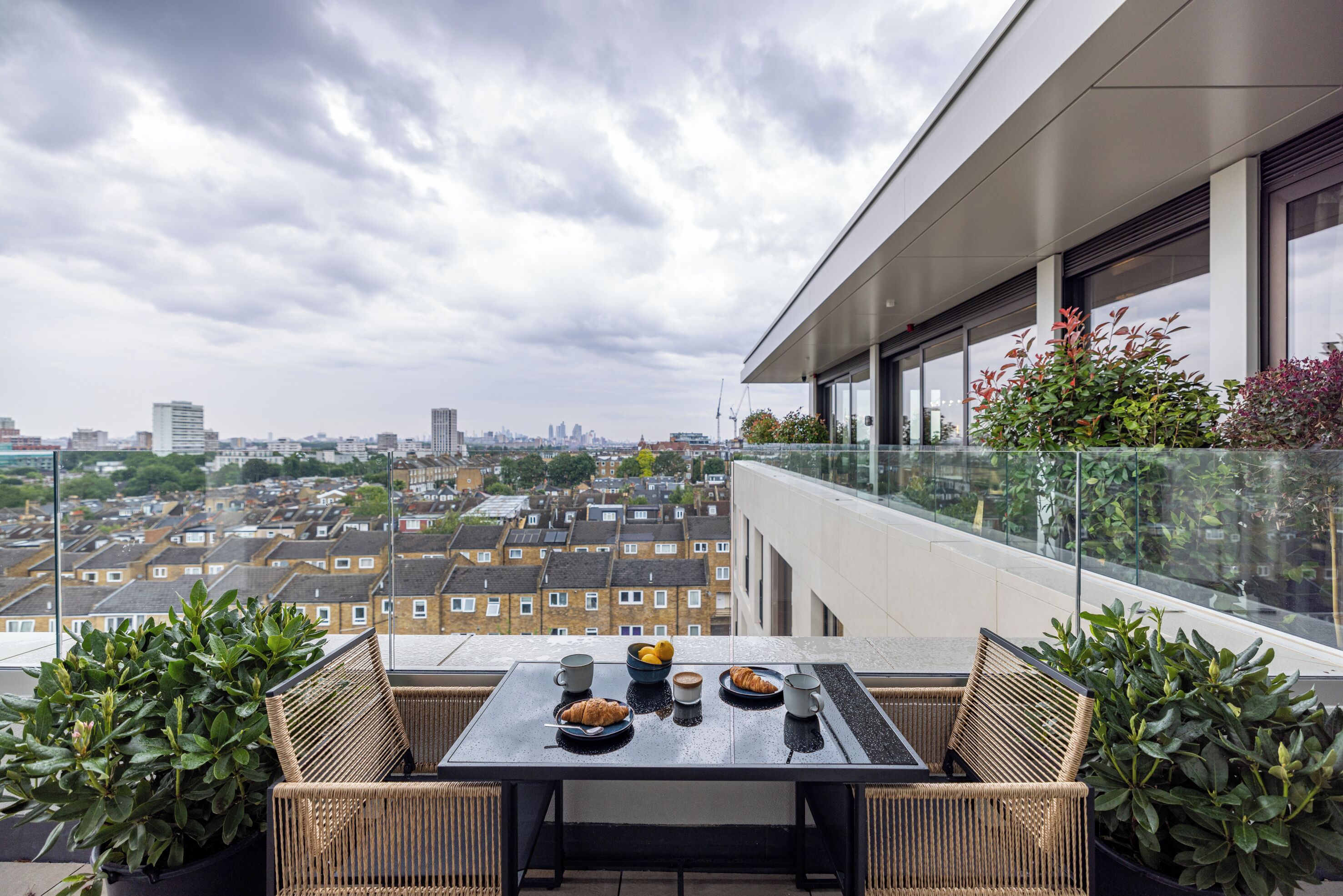 A balcony with a table set for two, overlooking a cityscape.