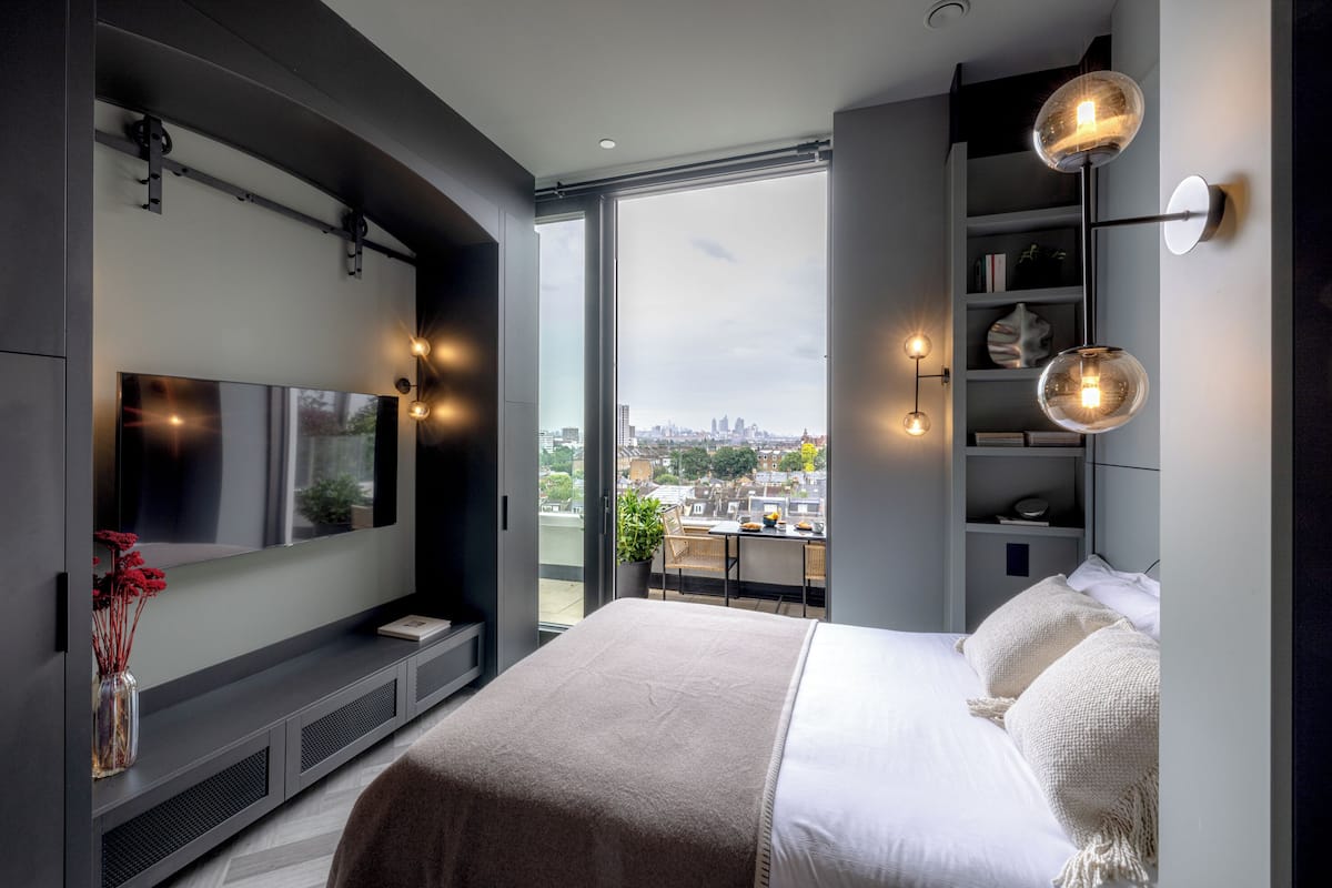 A modern bedroom with a large bed, a TV, and a city view.
