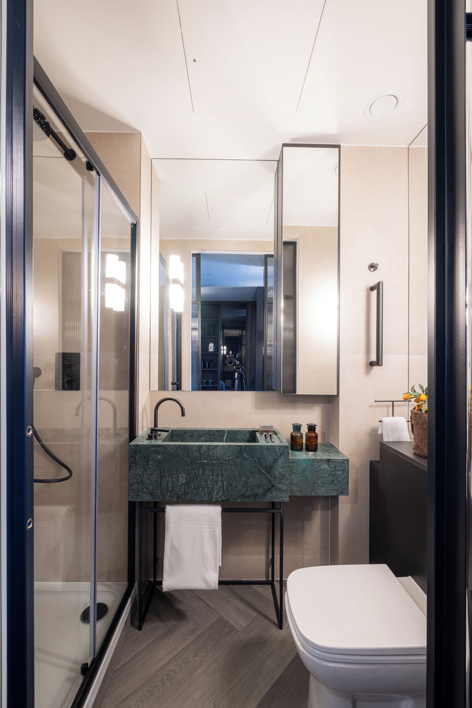 Un baño moderno con cabina de ducha de vidrio, lavamanos de mármol y un inodoro blanco.