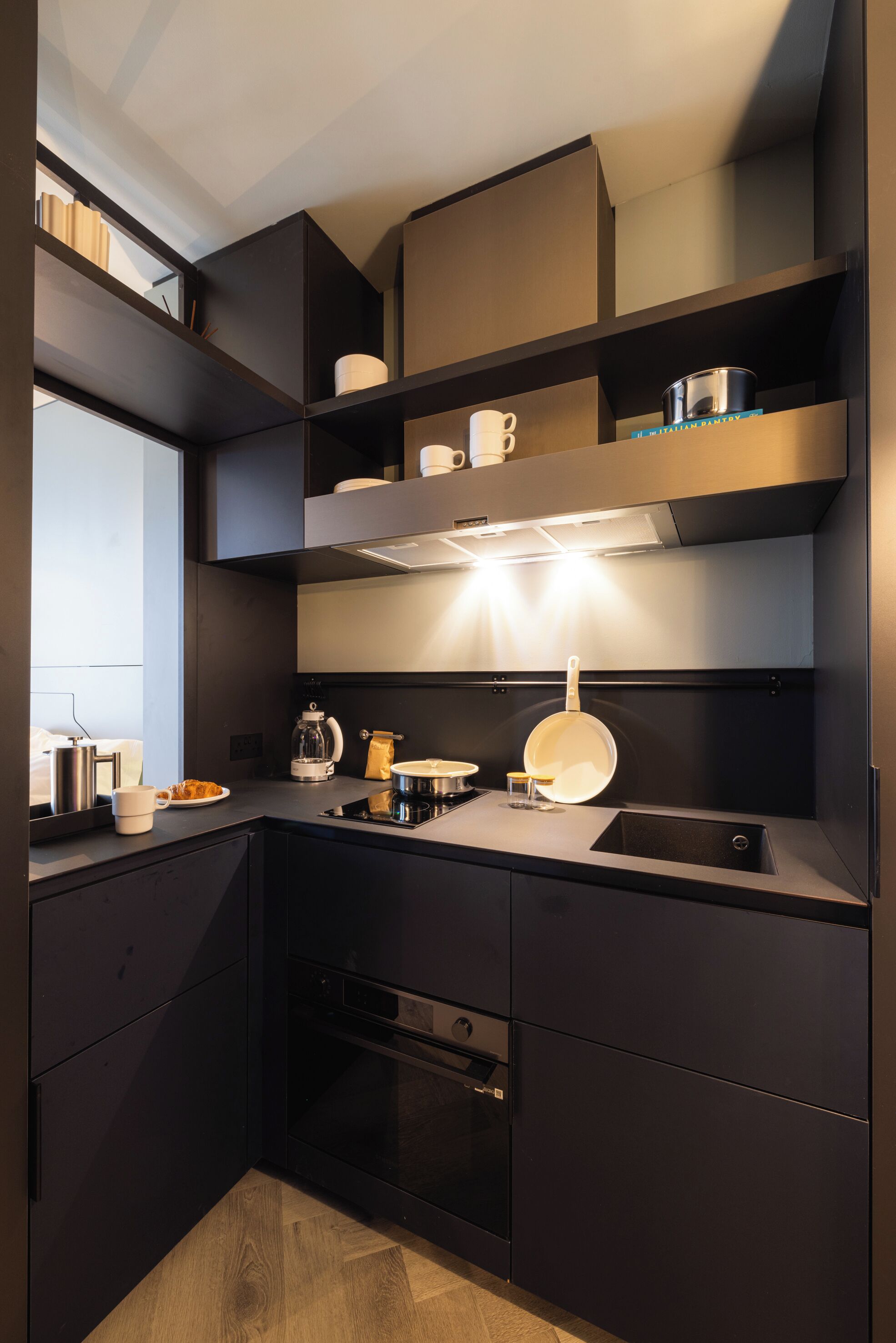 A modern kitchen with dark cabinetry, a built-in oven, and a stainless steel sink.