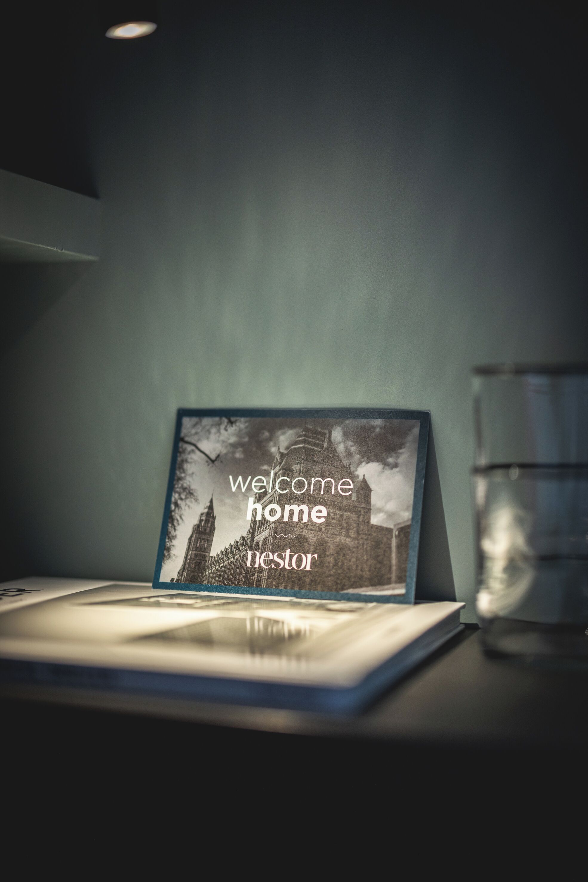 A framed welcome sign with a black and white photo of a building, placed on a table next to a glass of water.