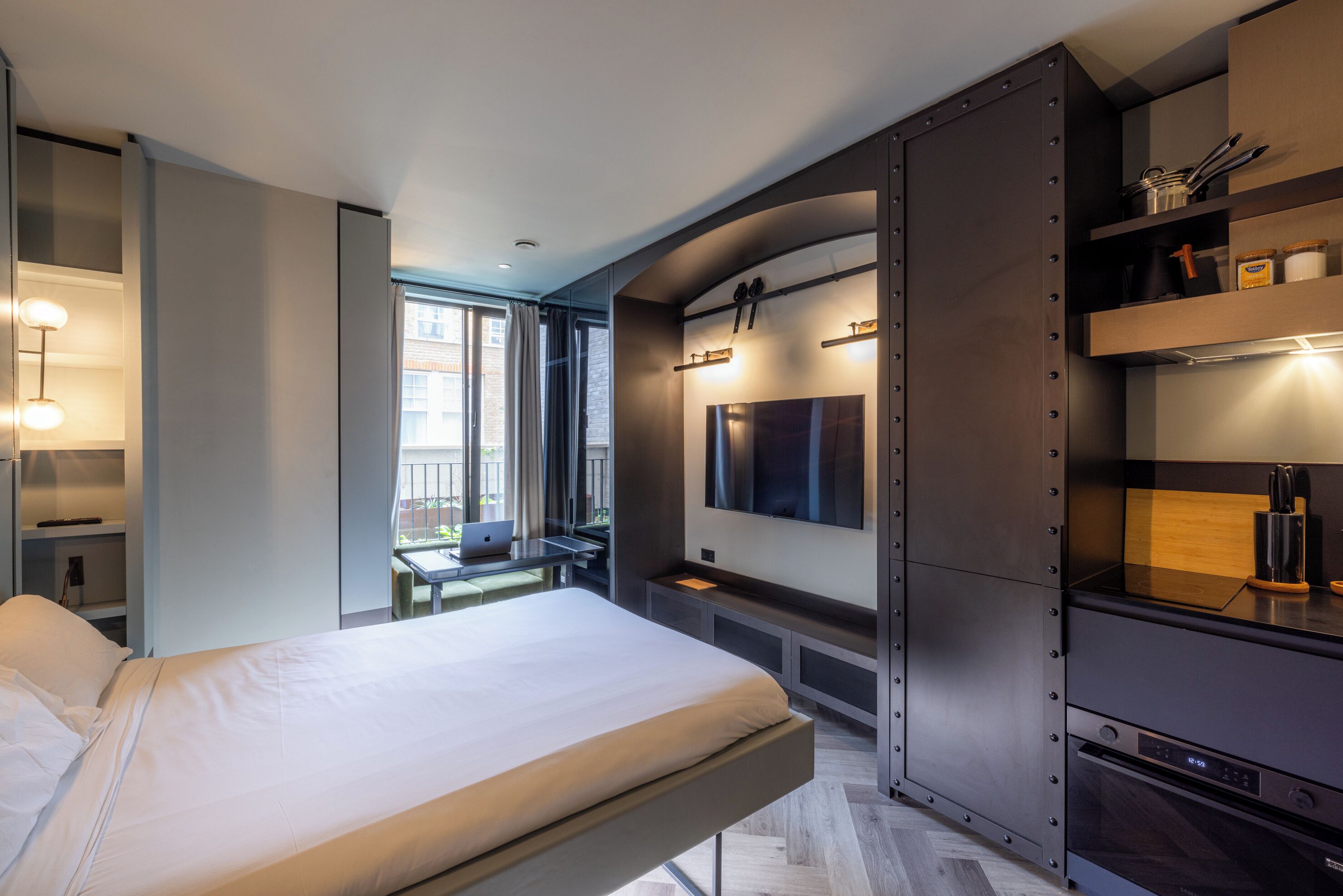 A modern hotel room with a bed, a desk with a laptop, a TV, and built-in cabinets.