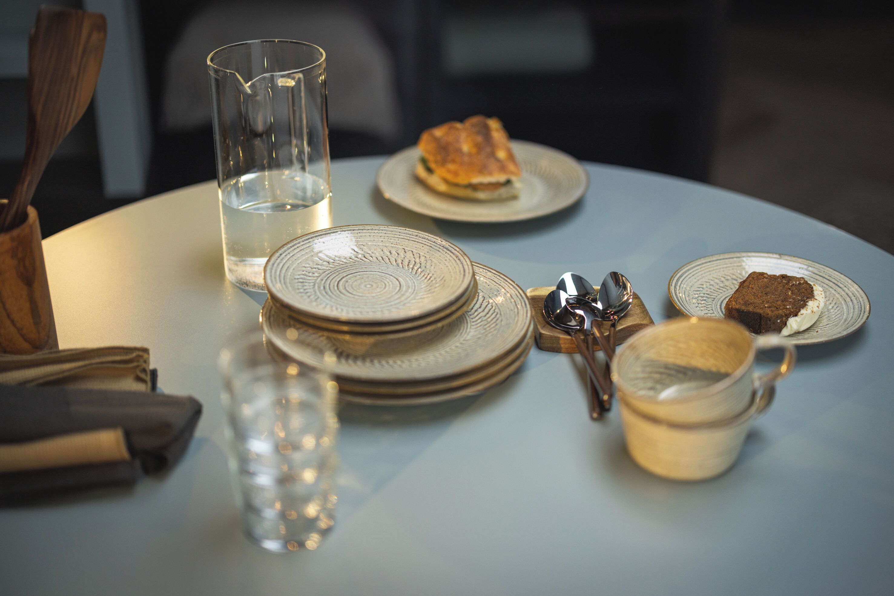Een tafel met borden, een glazen pitcher, een beker en een lepels.