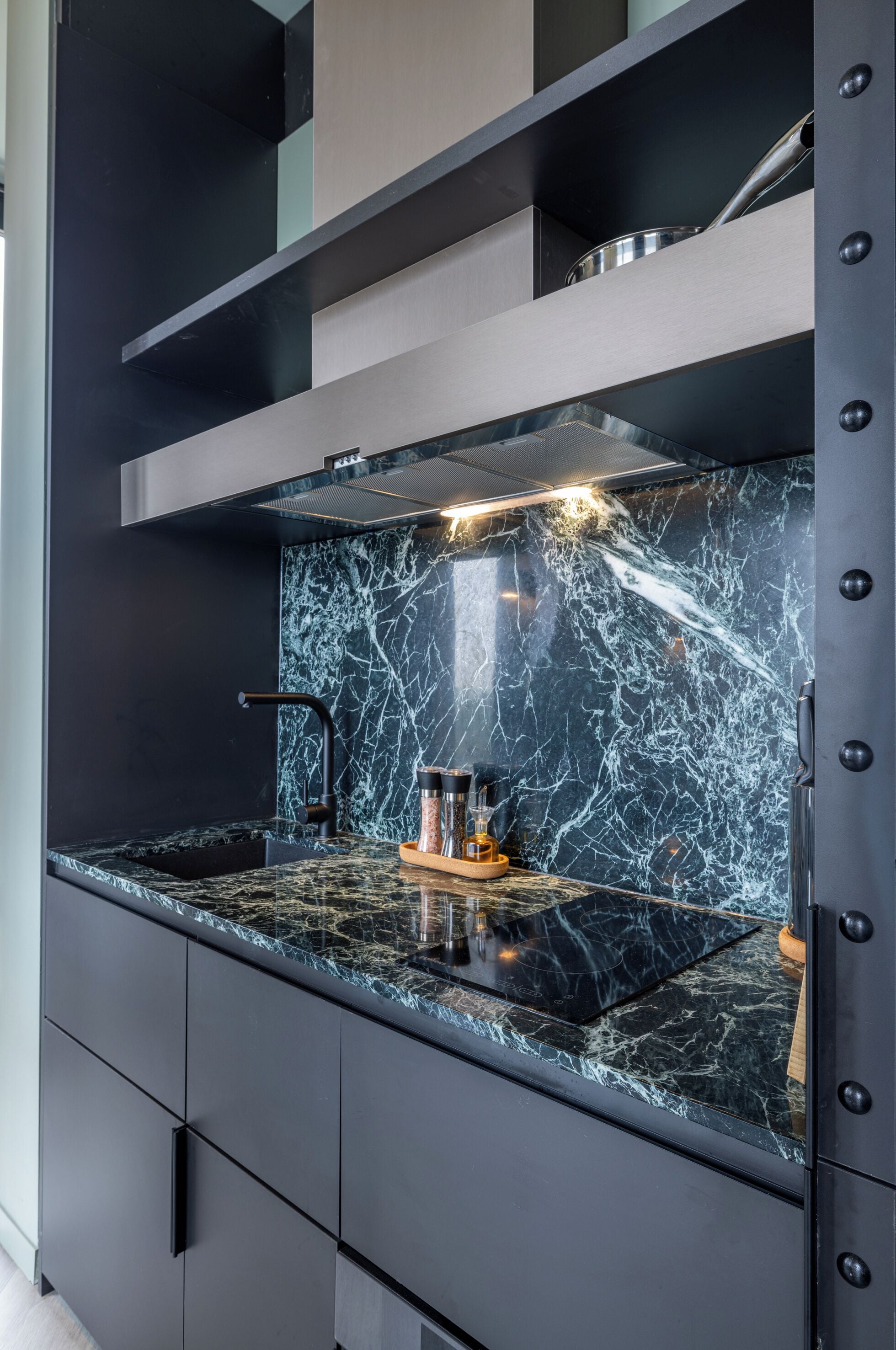 A modern kitchen with a black marble backsplash, stainless steel appliances, and black cabinetry.