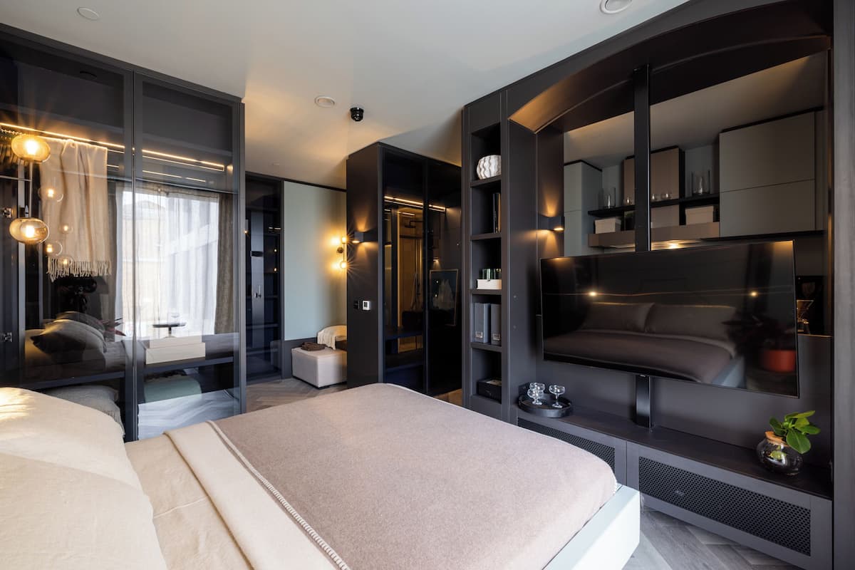A modern bedroom with a large bed, a TV, and built-in shelving.