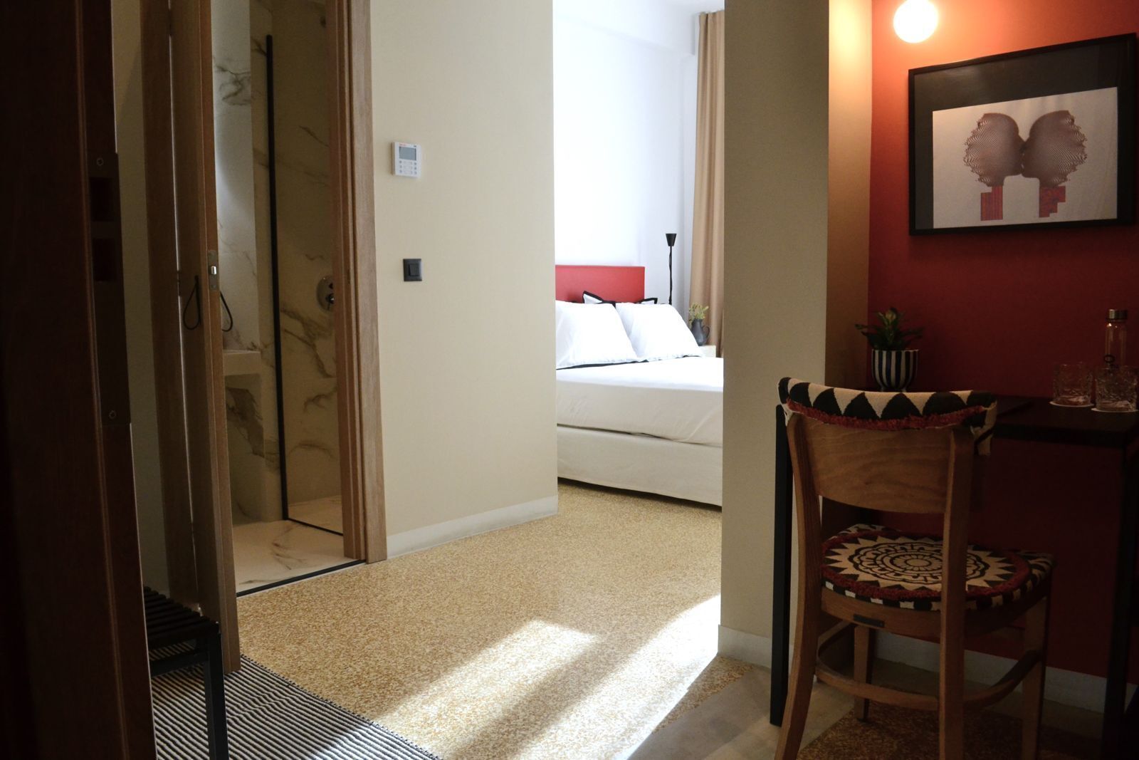 Quarto de hotel com uma cama, uma cadeira, uma mesinha e uma obra de arte na parede.
