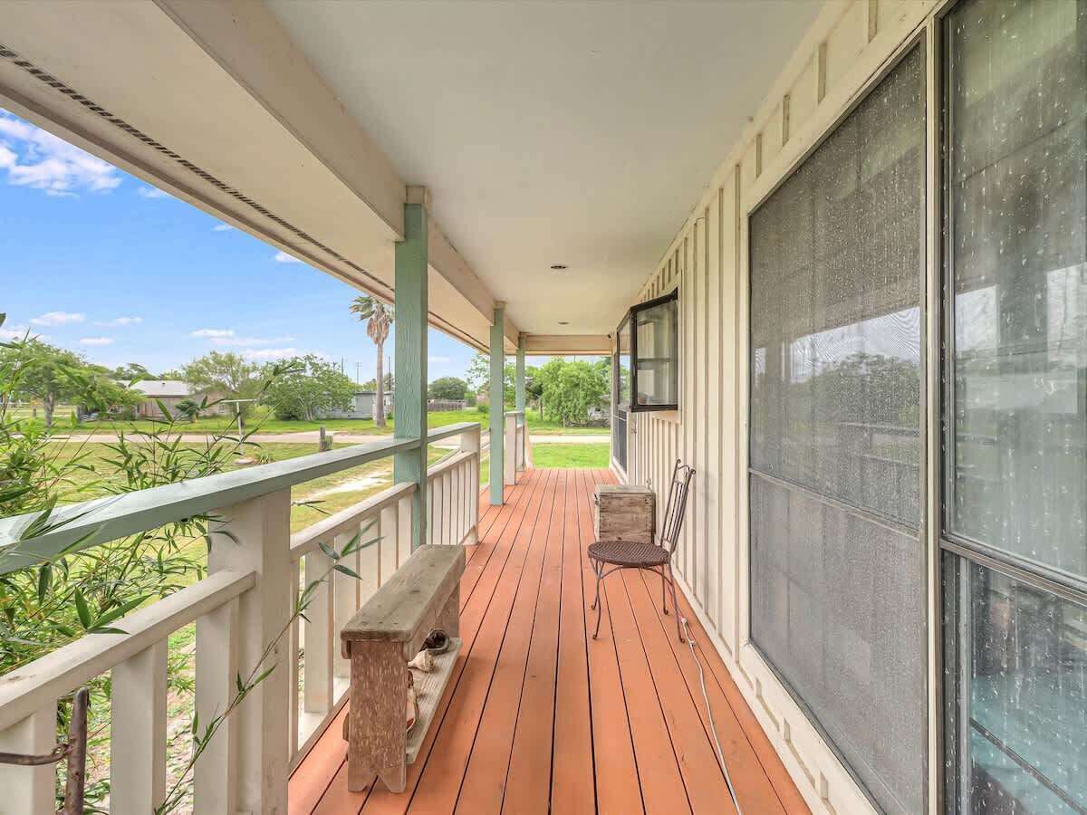 A covered porch with a bench and chair, a view of the outdoors, and a large window.