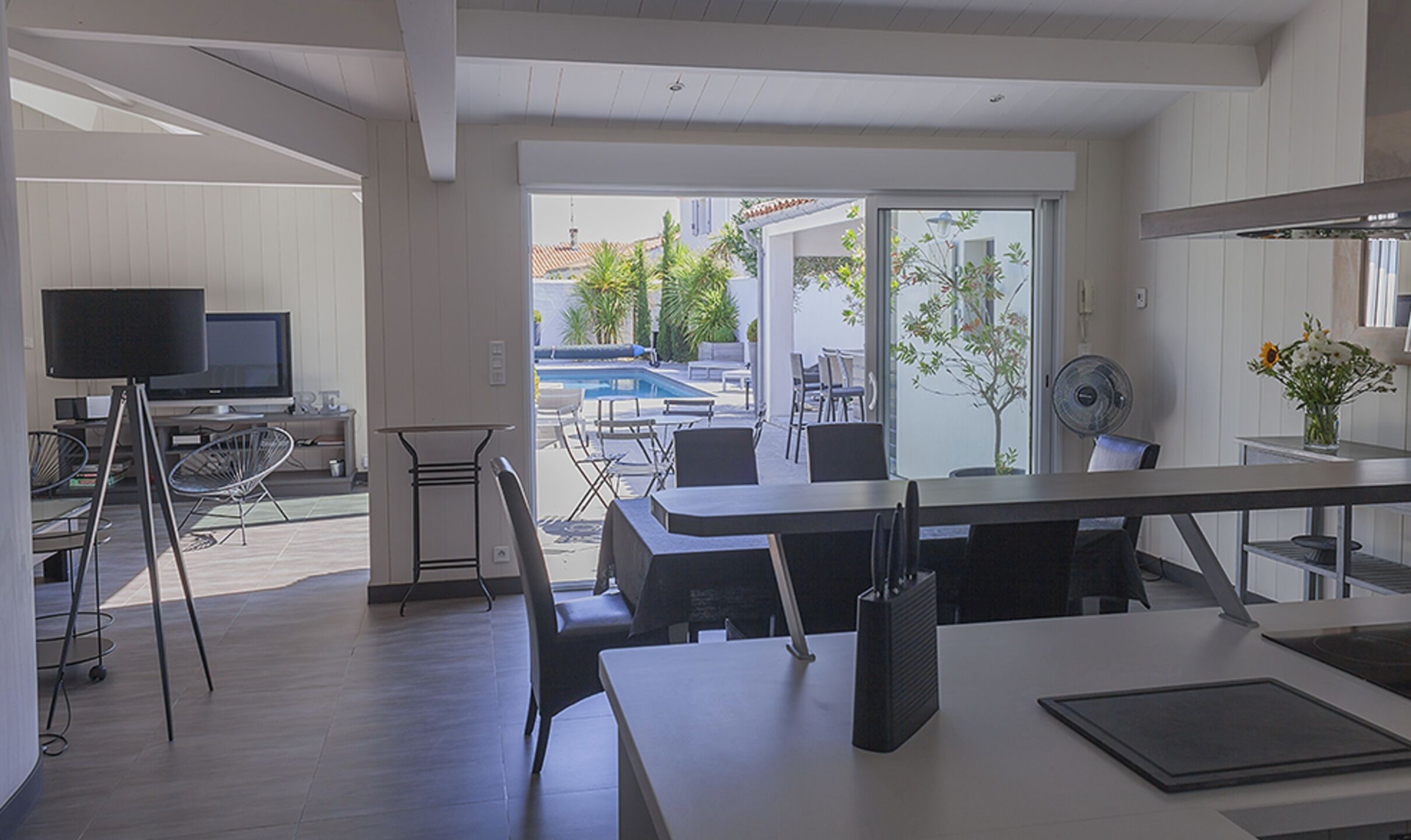A modern kitchen with a dining area, a TV, and a view of the outdoors.