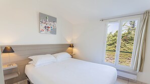 A bedroom with a large bed, two bedside lamps, a nightstand, a window with curtains, and a wall-mounted painting. - Maison Verte 4 Pers (LA FLOTTE)