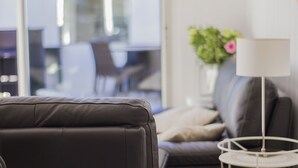 A modern living room with a leather sofa, a white lamp, and a vase with flowers. - Maison Verte 4 Pers (LA FLOTTE)