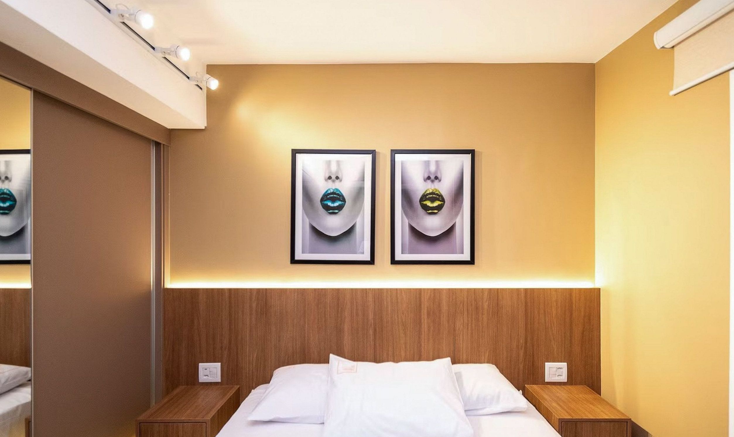 A hotel room with a wooden headboard, two bedside tables, a bed with white linens, and two framed artworks on the wall.