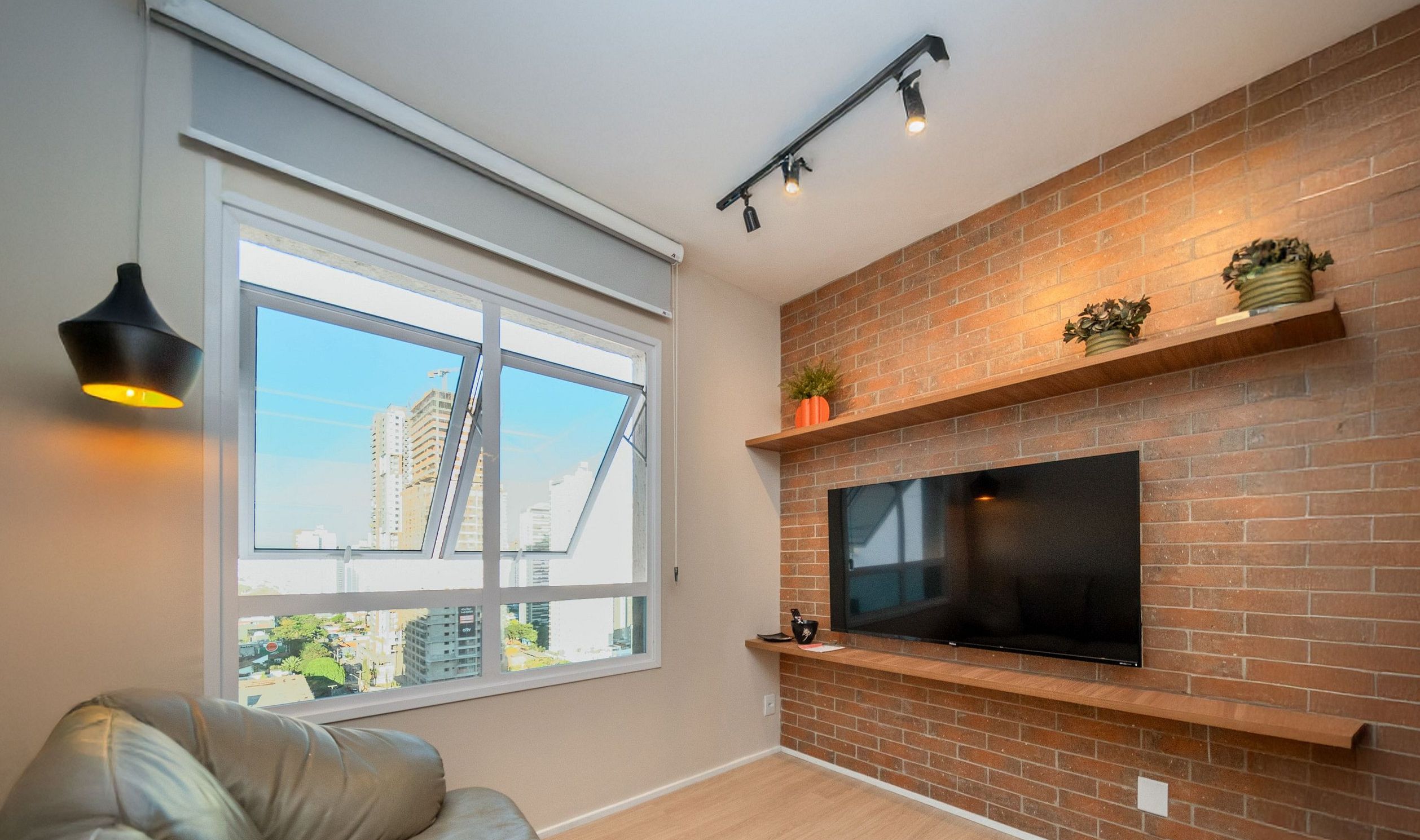 A modern living room with a large TV mounted on a brick wall, a window with a view of buildings, and a ceiling light fixture.