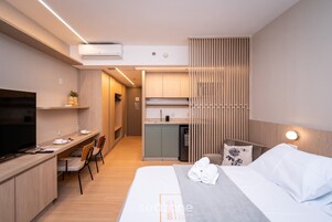 Habitación de hotel moderna con televisión, escritorio, kitchenette y cama con toallas.