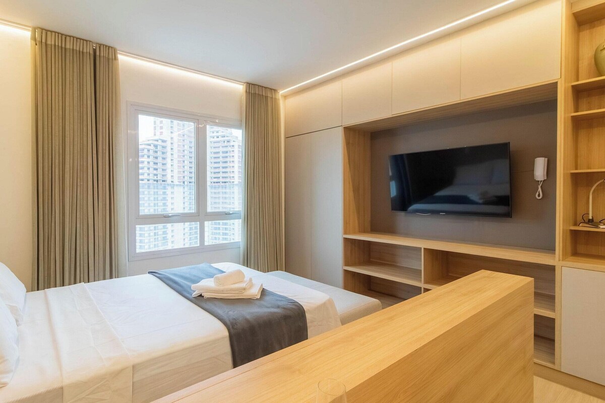 Une chambre d’hôtel avec un lit, une télévision, un bureau et une fenêtre avec des rideaux.