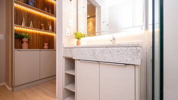 Un baño moderno con encimera de granito, un espejo grande y un mueble de tocador de madera con estantes.