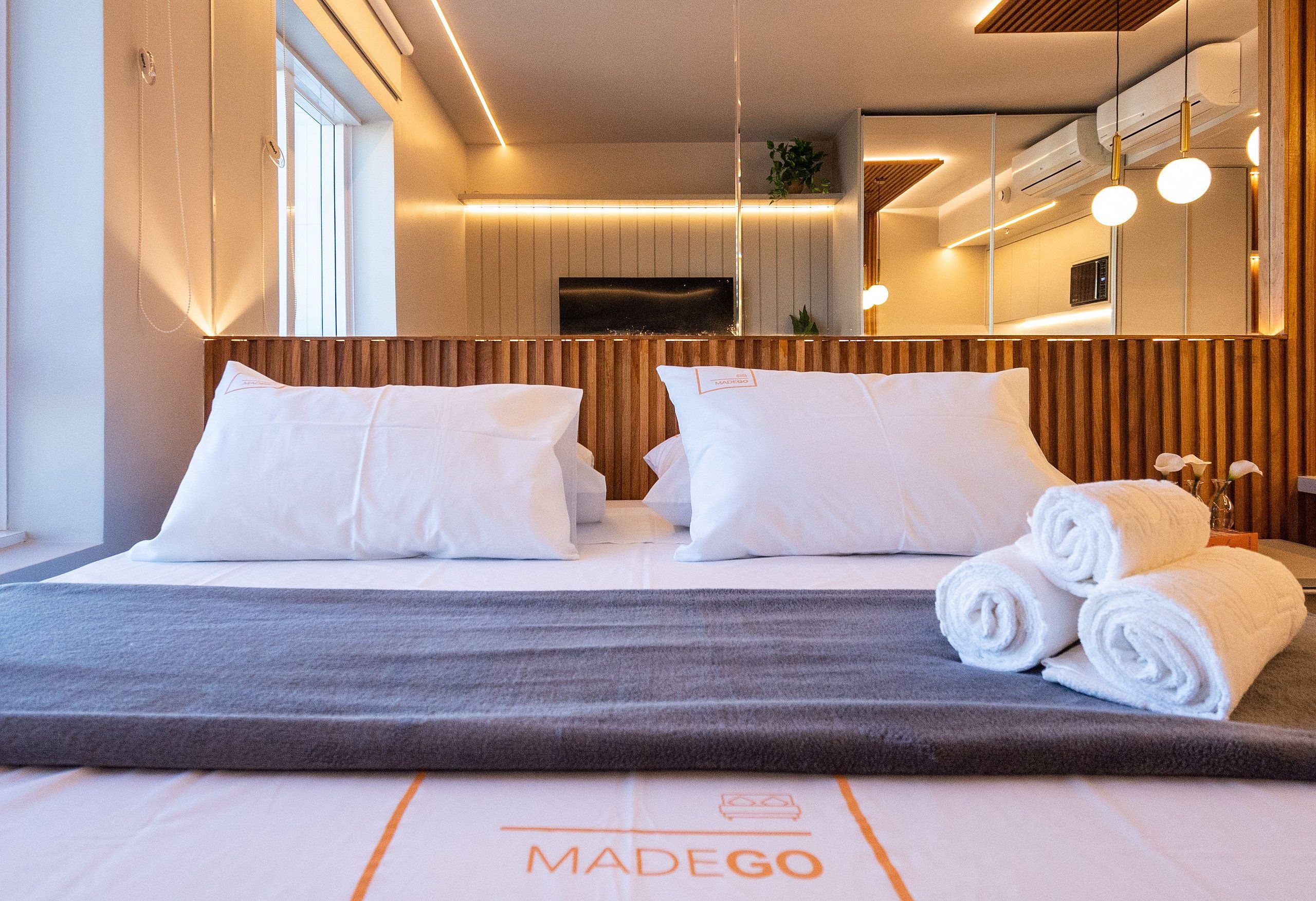 A hotel room with a bed, pillows, a grey blanket, and rolled towels.