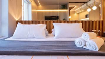 Una habitación de hotel con cama, almohadas, una manta gris y toallas enrolladas.