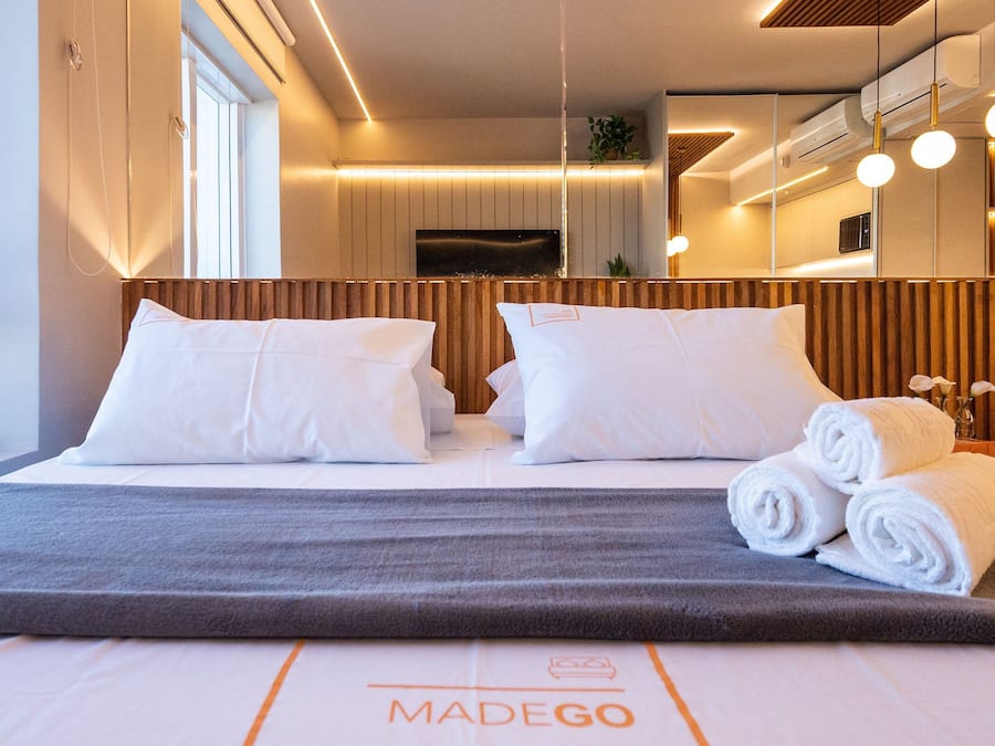 Une chambre d’hôtel avec un lit, des oreillers, une couverture grise et des serviettes enroulées.