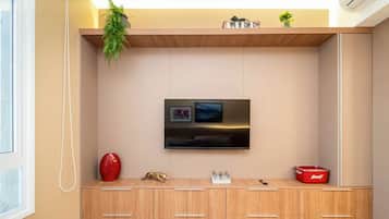 Uma sala de estar moderna com televisão de tela plana na parede, armários de madeira abaixo e um pequeno vaso vermelho à esquerda.