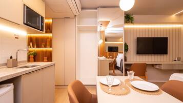Habitación de hotel moderna con cocina, comedor y televisor montado en la pared.