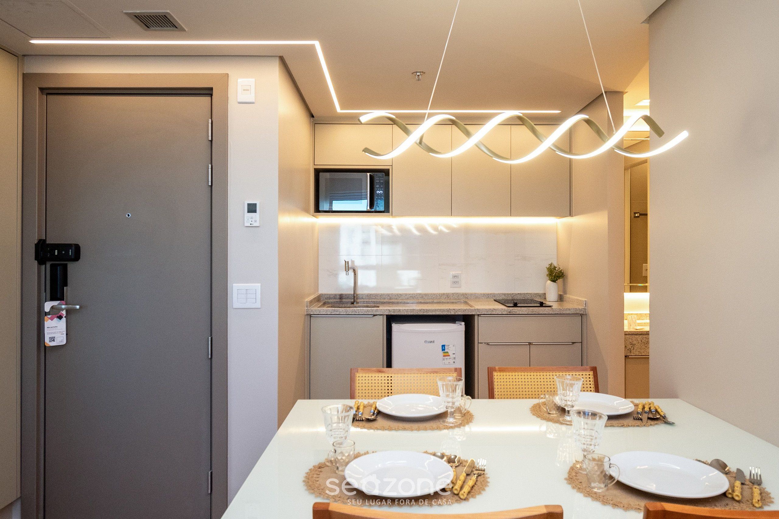 A modern dining area with a white table set for four, a microwave, and a refrigerator in the background.