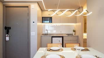 A modern dining area with a white table set for four, a microwave, and a refrigerator in the background.