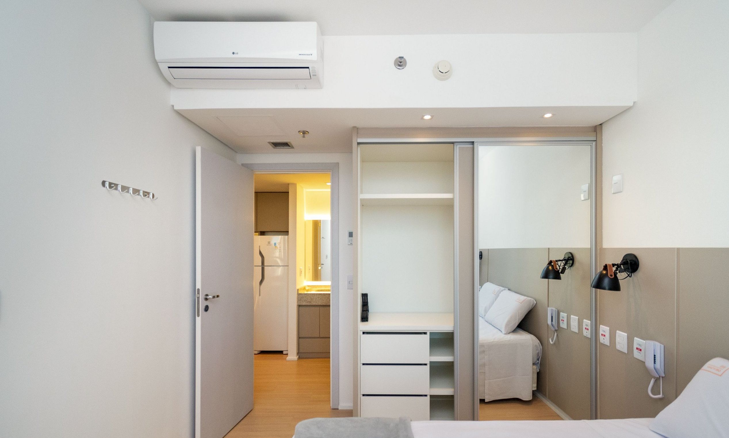 Quarto de hotel com cama, guarda-roupa, secretária e banheiro visível por uma porta aberta.