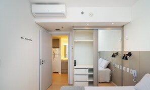 Habitación de hotel con cama, armario, escritorio y baño visible a través de una puerta abierta.