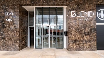 Ein moderner Gebäudeeingang mit Glastüren, einer Marmorfassade und Beschilderung für 'EBM 95' und 'BLEND Smart Style'.