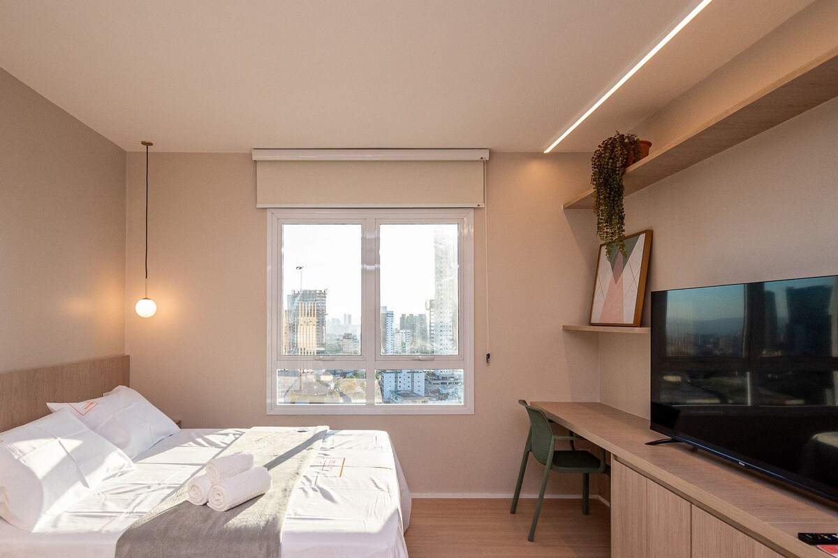 Une chambre d’hôtel moderne équipée d’un lit, d’un bureau, d’une télévision et d’une fenêtre donnant sur la ville.